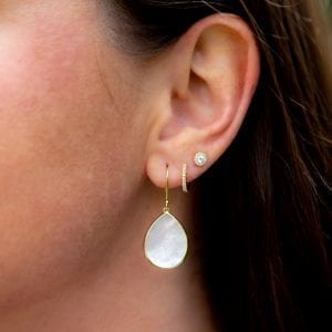 womand ear with gold and mother of pearl teardrop earring, tiny diamond hoop and round diamond halo earring