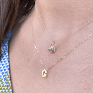 two gold pendant necklaces layered on Women's right angled view of neckline