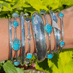 stack of silver and turquoise bracelets on wrist with green background