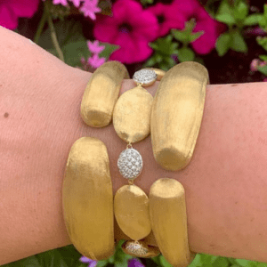 three gold bracelets on wrist with floral background