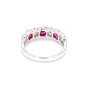 Back view of ring. A simple white gold band leads to a seven stone setting that holds three oval rubies and four round brilliant cut diamonds, framed by scalloped pave diamond edges.