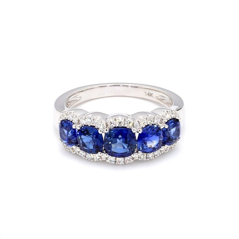 Front view of ring. Five round sapphires are set along the front half of a simple white gold band framed by pave diamond scalloped edges.