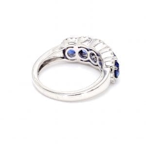 135 degree angle of ring. A simple white gold band leads to a setting that holds five round sapphires framed by pave diamond scalloped edges.