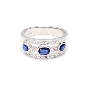 Front view of this ring with a thick white gold band, the center front has cut outs with a row of alternating bezel set oval sapphires and round diamonds. The top and bottom bands of the front half of this ring is accented by pave diamonds.