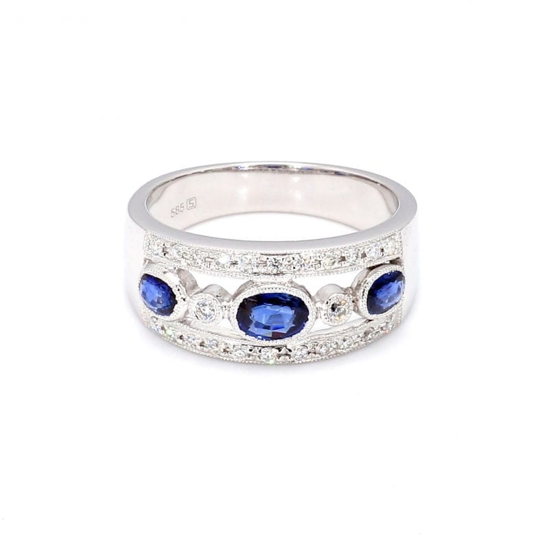 Front view of this ring with a thick white gold band, the center front has cut outs with a row of alternating bezel set oval sapphires and round diamonds. The top and bottom bands of the front half of this ring is accented by pave diamonds.