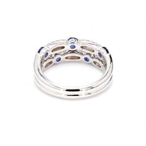Back view of ring. A double white gold shank attaches to the setting of double rows of pave diamond stations and round sapphires offset from each other.