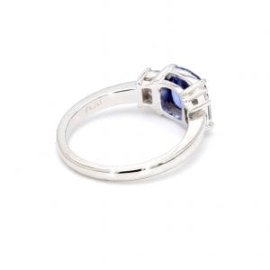 135 degree angle of ring. A simple white gold band leads to the setting for a three stone ring with a cushion cut sapphire center and an emerald cut diamond on either side.
