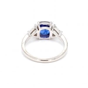 Back view of ring. A simple white gold band leads to a three stone setting with a cushion cut sapphire in the center and a trillion cut diamond on either side.