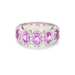 Front view of ring. A row of five oval cut pink sapphires are set along the front half of the band with pave diamond halos around each.