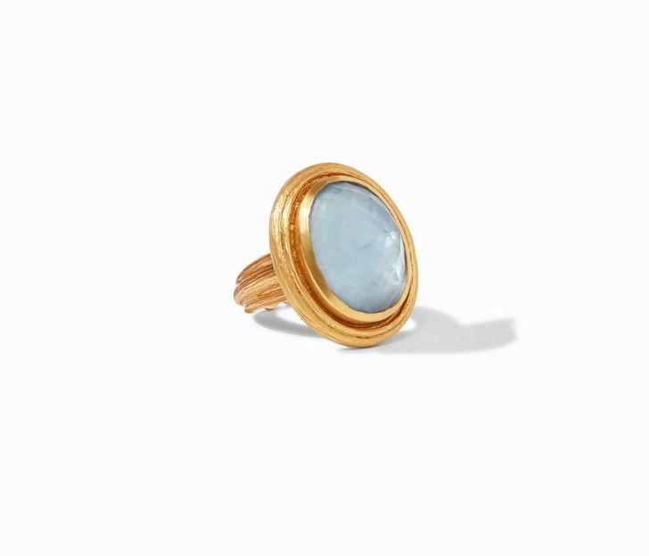 45 degree angle of ring. A domed, oval blue chalcedony gemstone is haloed by textured 24kt gold with a matching textured shank.
