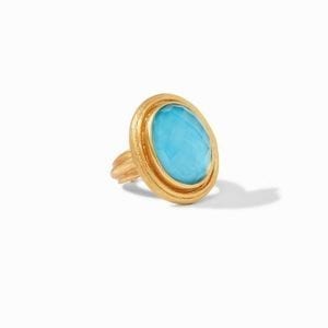 45 degree angle of ring. An oval, domed pacific blue stone center is haloed by a textured frame of gold plating, Attached to a matching textured and plated shank.