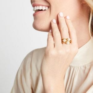 A set of three. Three stackable rings feature a textured gold plated band with a pearl in the center. This set is pictured on the middle finger of a laughing woman who is lightly touching her jawbone.