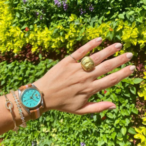 gold rings, turquoise and leather watch, and gold and diamond bracelets on model with floral background
