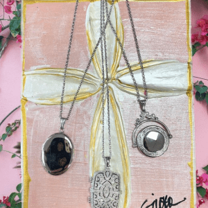three silver locket necklaces on pink background