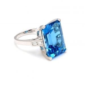 45 degree angle of ring. An octagonal step-cut blue topaz sits in the center of a polished white gold band with two diamond baguettes accenting each shoulder of the shank.