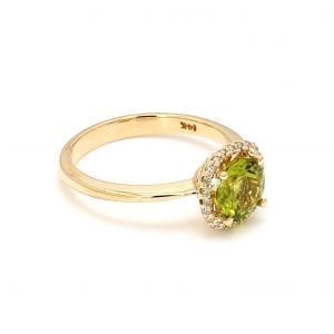 45 degree angle of ring. A center, light green peridot is surrounded by a halo of diamonds, complimented by a polished yellow gold shank.