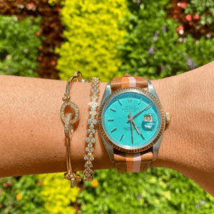 brown and turquoise watch and two gold bracelets on wrist with green foliage background