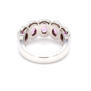 Back view of ring. A simple white gold band leads to a five stone oval setting that has five pink sapphires with pave diamond halos.
