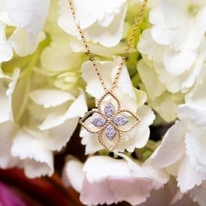 gold and diamond necklace hanging in front of white flowers