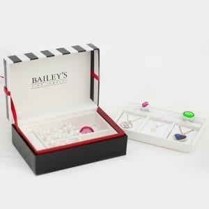 Plastic ring inside of jewelry box with black bottom, white interior, and a black and white striped top. Next to the box is a white insert that goes in the box. it has jewelry on it.