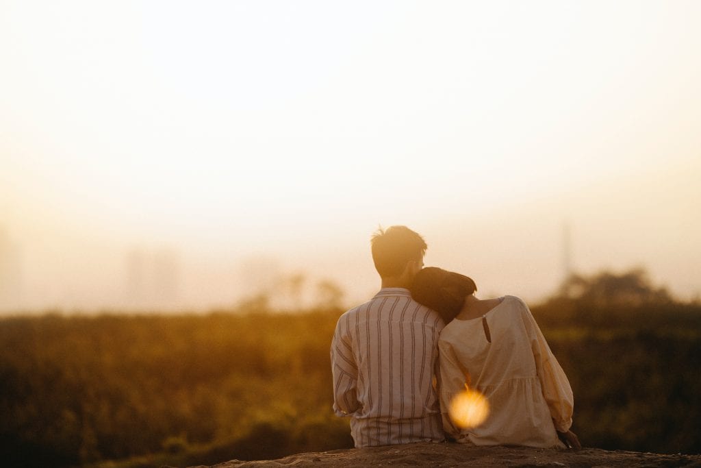 Couple sitting together in a field with their backs to the camera.