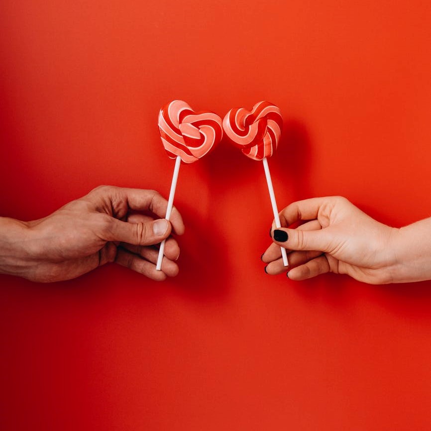 Two hands holidy striped heart shaped lollipop candies.