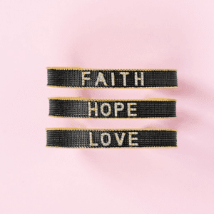 3 black bracelets that say faith. hope. and love, on pink background