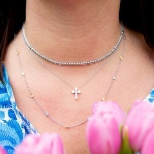 woman's neck in blue and white dress holding pink tulps wearing diamond tennis necklace, diamond cross necklace and diamond station necklace